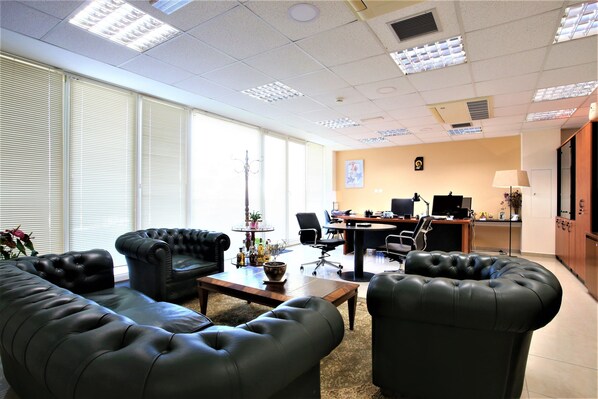 A spacious office with leather sofas, a wooden coffee table, and a desk area with computers.