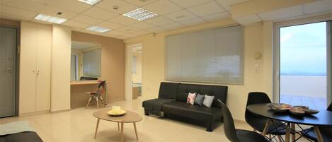 A modern living room with a sofa, a dining table, and a kitchen area in the background.