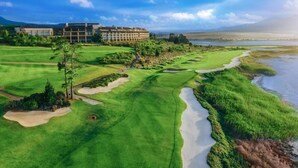 Un campo de golf con búnkeres, un obstáculo acuático y un edificio al fondo.