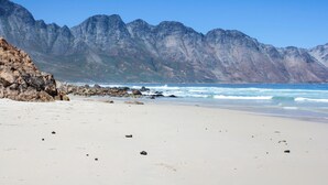 Uma praia com afloramentos rochosos e montanhas ao fundo.