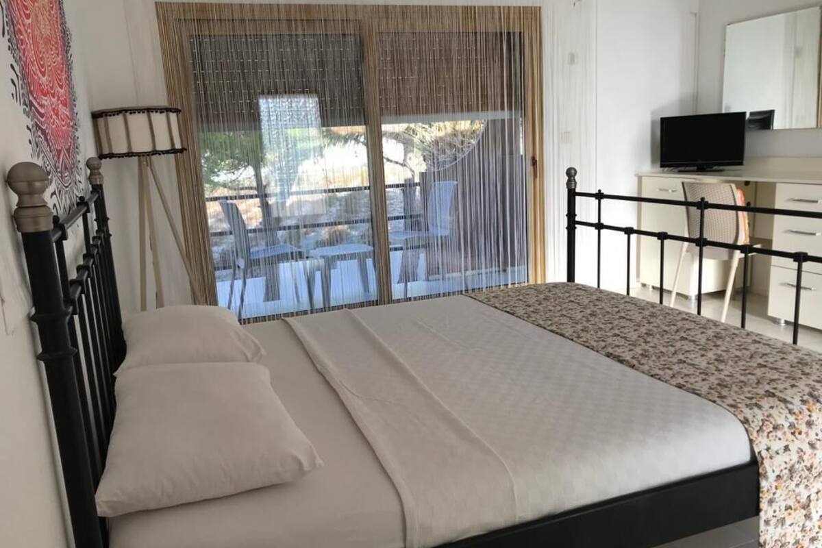 A bedroom with a bed, a desk, a chair, a television, and a window with curtains.
