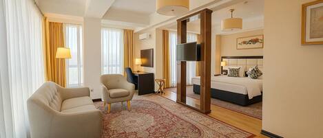 Une chambre d’hôtel avec un grand lit, un coin salon avec un fauteuil, un bureau et une télévision.