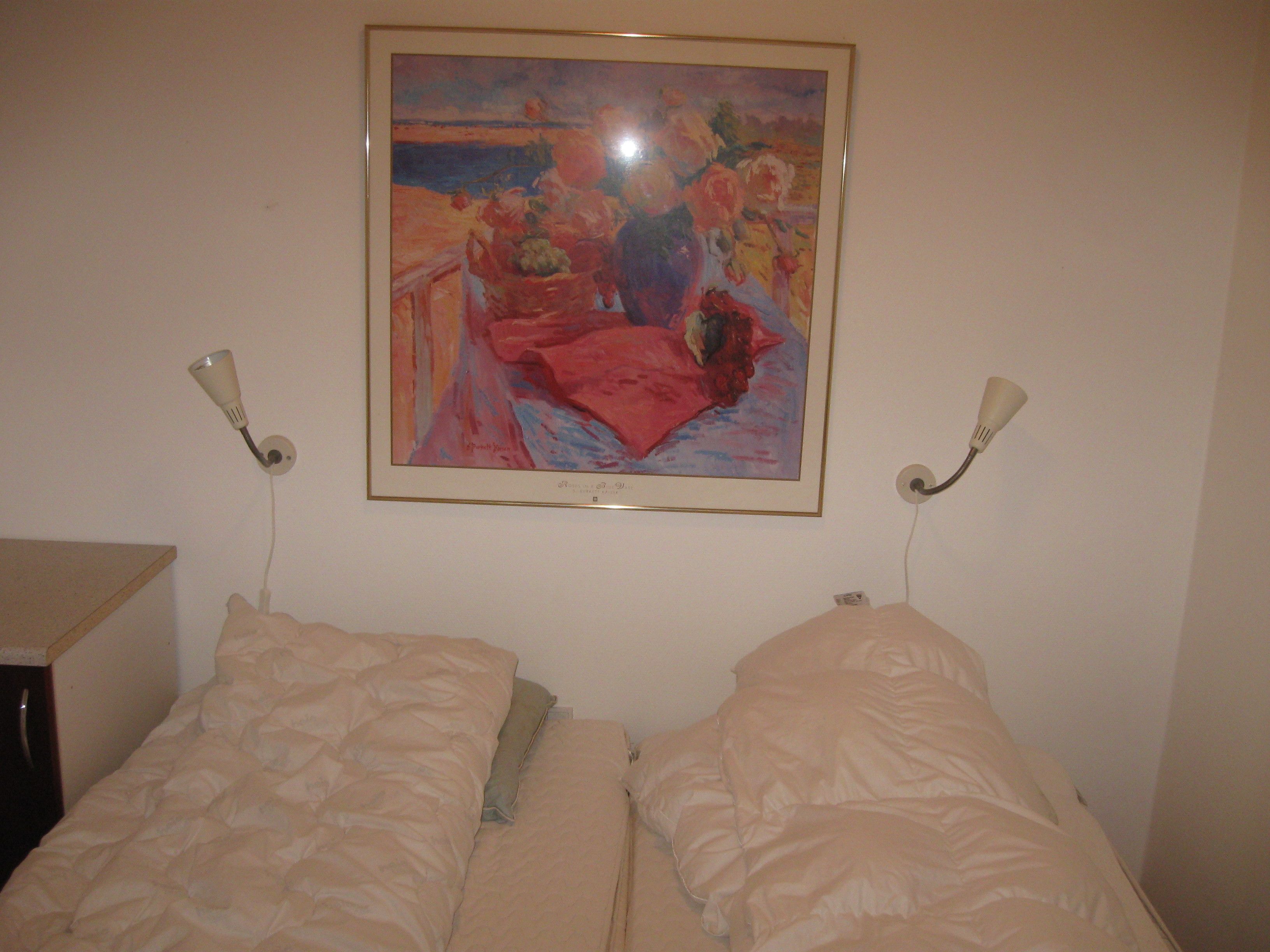 A bedroom with two beds, a painting on the wall, and bedside lamps.