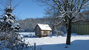 A wooden cabin with a snow-covered roof, surrounded by snow-laden trees and bushes. - Koebenhovedskov Bed & Breakfast (Rodding)