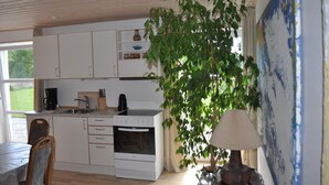 A kitchen with white cabinets, a stove, and a sink. There is a dining table with chairs and a large plant. - Koebenhovedskov Bed & Breakfast (Rodding)
