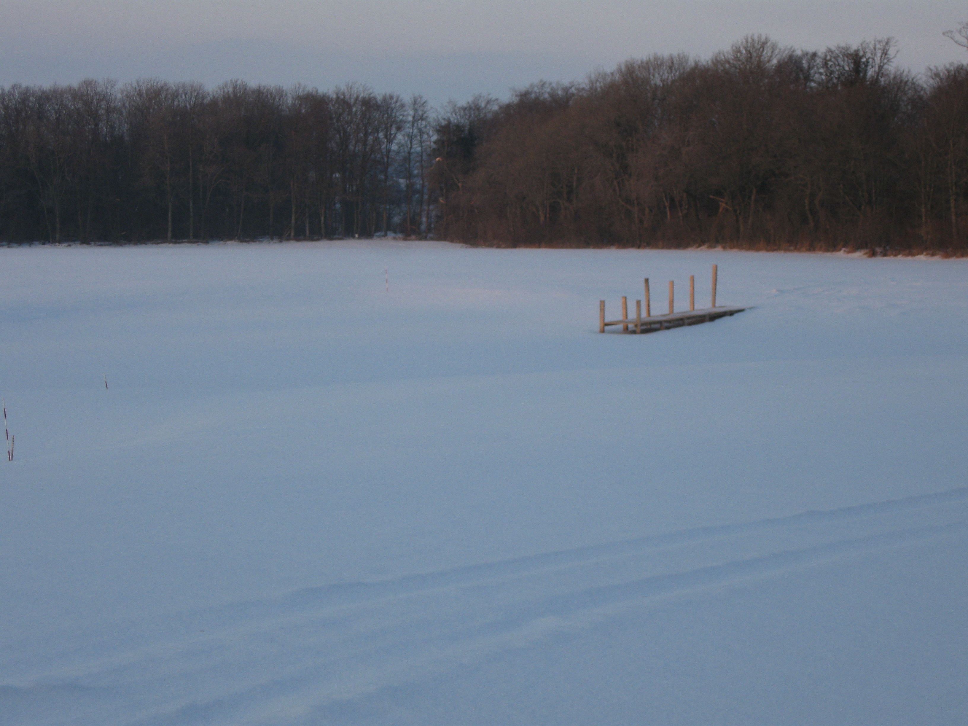 A snowy landscape with a wooden dock extending into a frozen body of water.