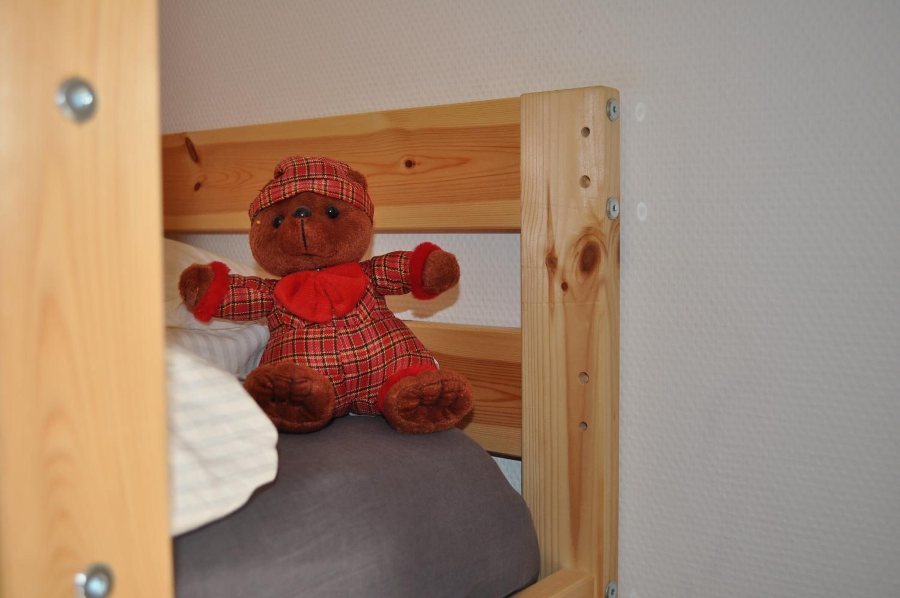 A wooden bunk bed with a plush teddy bear dressed in a plaid outfit sitting on the lower bunk.