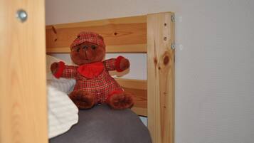 A wooden bunk bed with a plush teddy bear dressed in a plaid outfit sitting on the lower bunk.