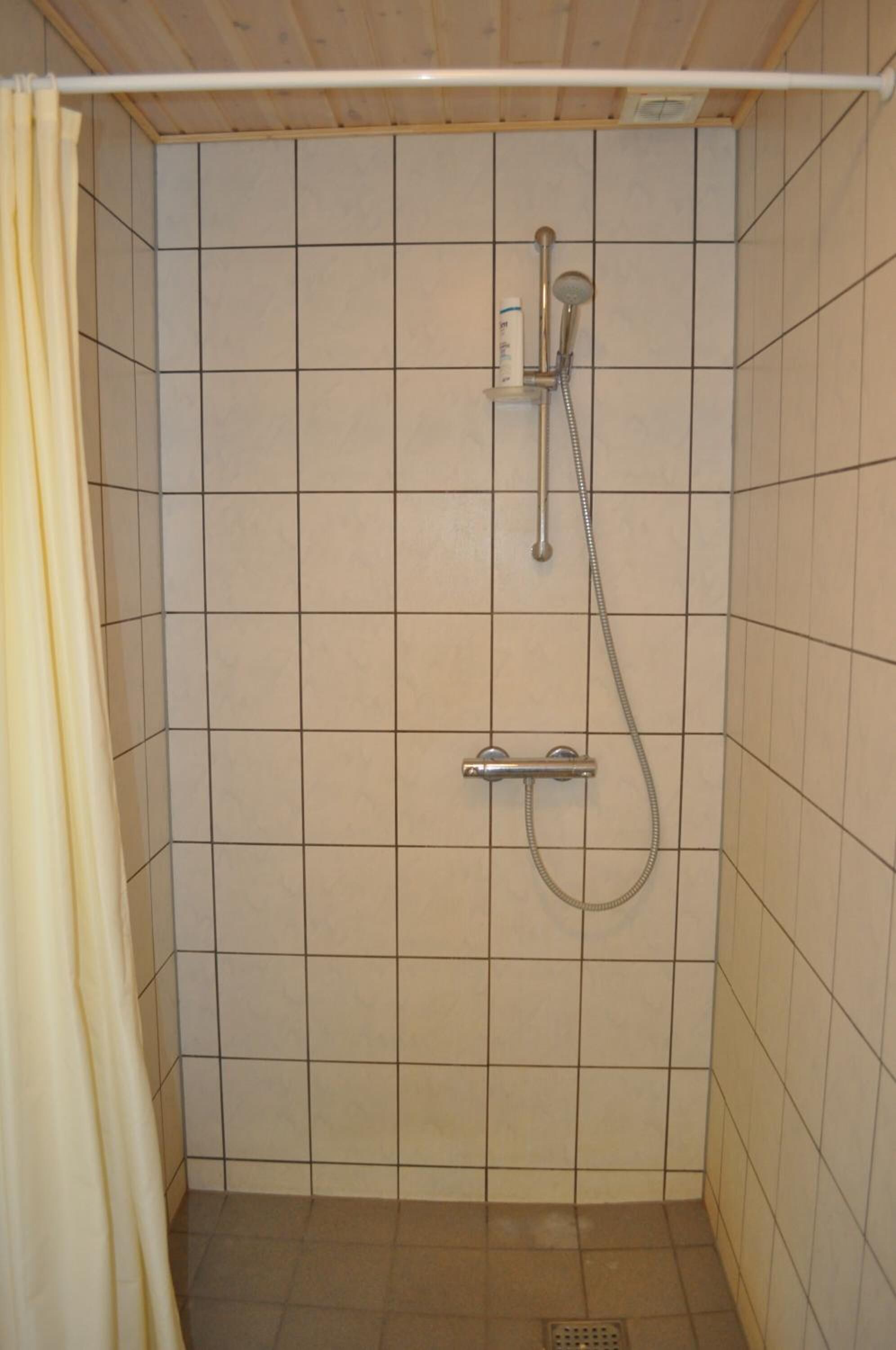 A small, tiled shower area with a showerhead and control panel.