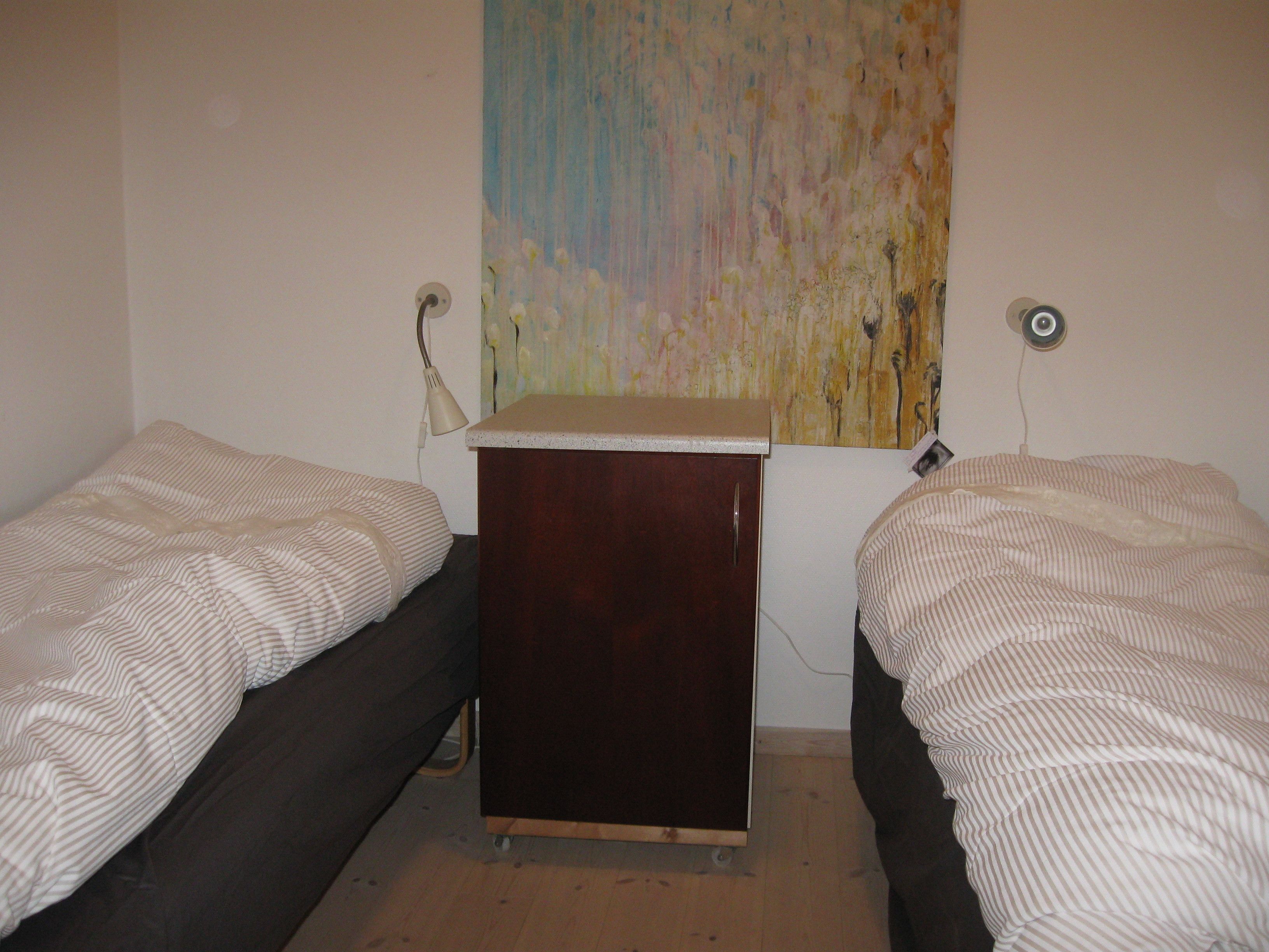 Une chambre avec deux lits simples, un petit bureau en bois et une lampe fixée au mur.