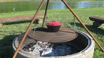 A portable outdoor grill with a pot on top, set up on a grassy area near a body of water.