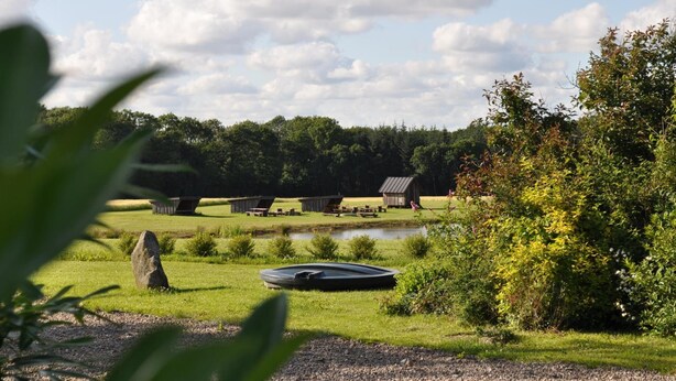 A serene lakeside setting with rustic cabins, a small dock, and lush greenery. - Koebenhovedskov Bed & Breakfast (Rodding)