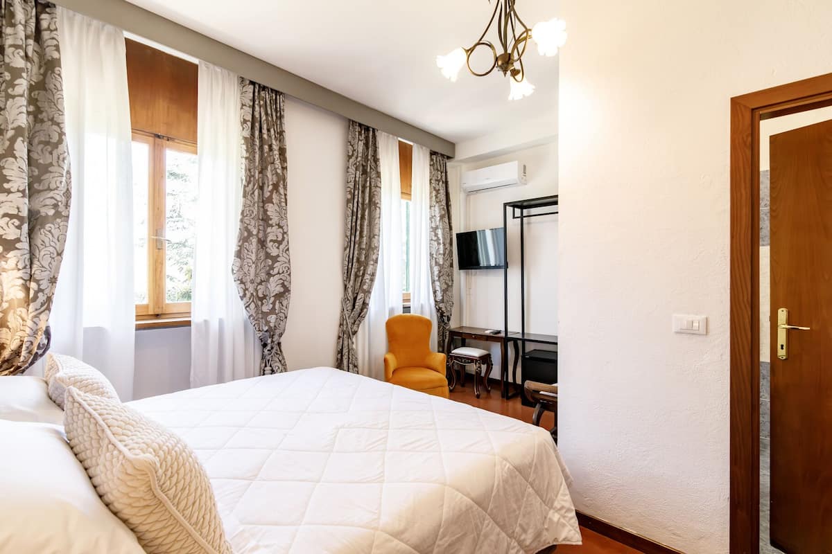A hotel room with a large bed, a desk with a chair, a television, and a door.