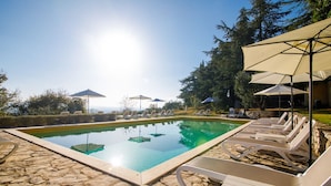 A pool with lounge chairs and umbrellas, surrounded by stone tiles and trees. - Agriturismo Villa Godenano - Pool & Restaurant (Castellina in Chianti)