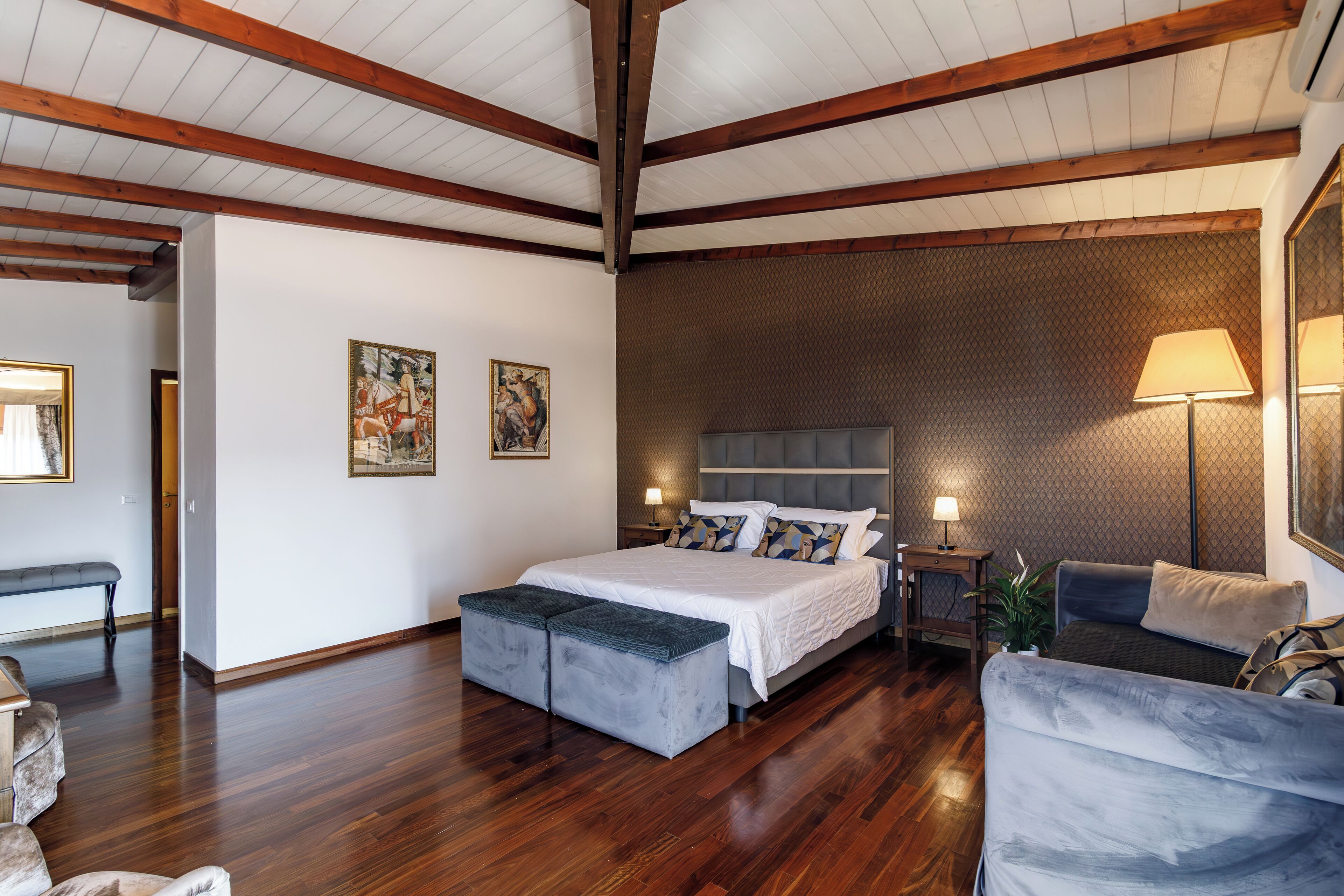 Ein geräumiges Schlafzimmer mit einem großen Bett, einer Bank, einem Sessel und einem Nachttisch mit Lampe.