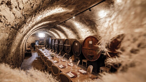 A long table set for dining in a tunnel with wine barrels on one side. - Agriturismo Villa Godenano - Pool & Restaurant (Castellina in Chianti)