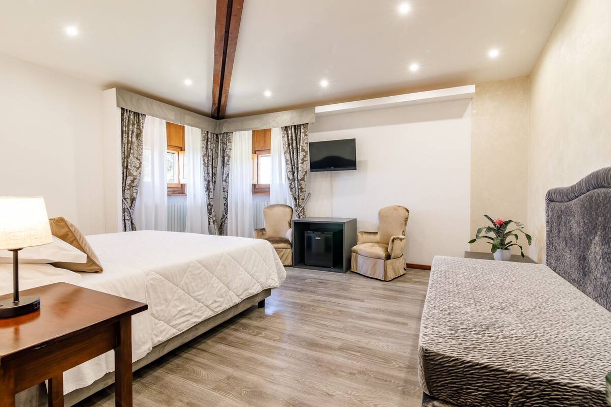 A hotel room with a bed, a desk, a chair, a TV, and a small table with a plant.