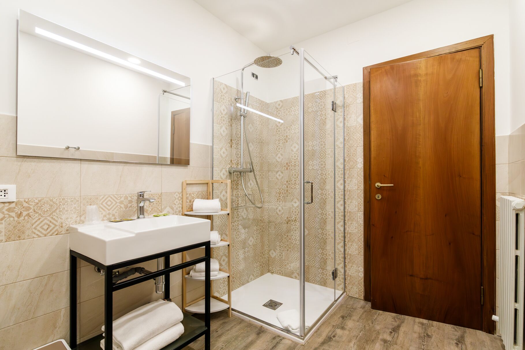 Ein Badezimmer mit einer Duschkabine, einem Waschbecken mit Spiegel darüber und einer Holztür.