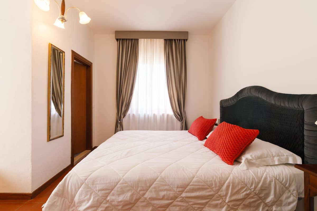 A neatly made bed with a white quilt, two red pillows, and a dark headboard.