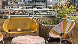 A rooftop terrace with wicker furniture and a view of city buildings. - The Buxton (London)