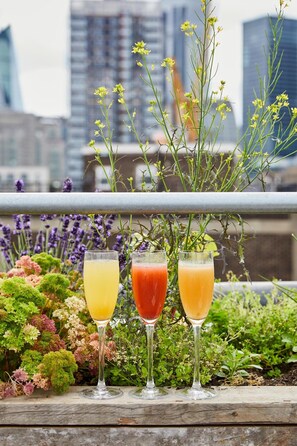 Three glasses of beverages on a balcony with a cityscape in the background. - The Buxton (London)