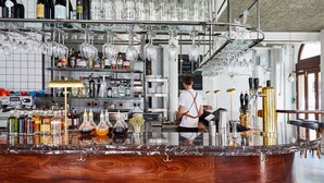 A bar area with a wooden counter, shelves with bottles, and hanging glasses. - The Buxton (London)