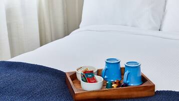 Ein hölzernes Tablett mit einer Kaffeemaschine, zwei Tassen und einer Taschentuchbox auf einem Bett.