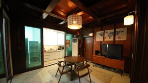 Uma sala de jantar com uma mesa e cadeiras de madeira, um lustre e uma televisão sobre um suporte de madeira.