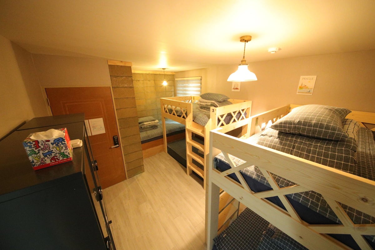 A dormitory room with bunk beds, a desk, and a small kitchenette.