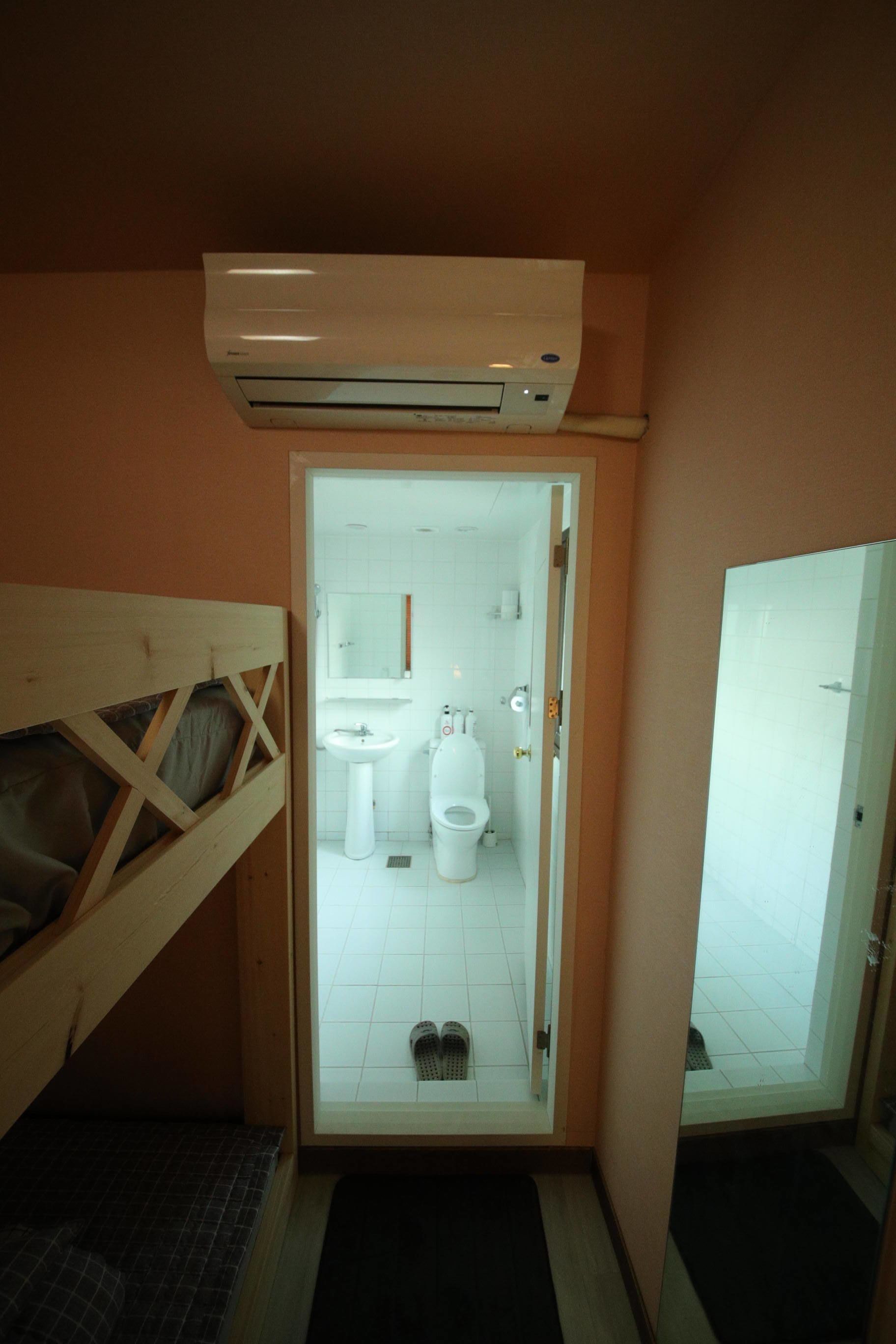 A small, compact bathroom with a wooden bunk bed, a white sink, a toilet, and a mirror.