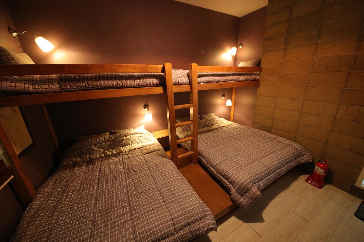 A bunk bed room with two beds, a ladder, and wall-mounted lights.