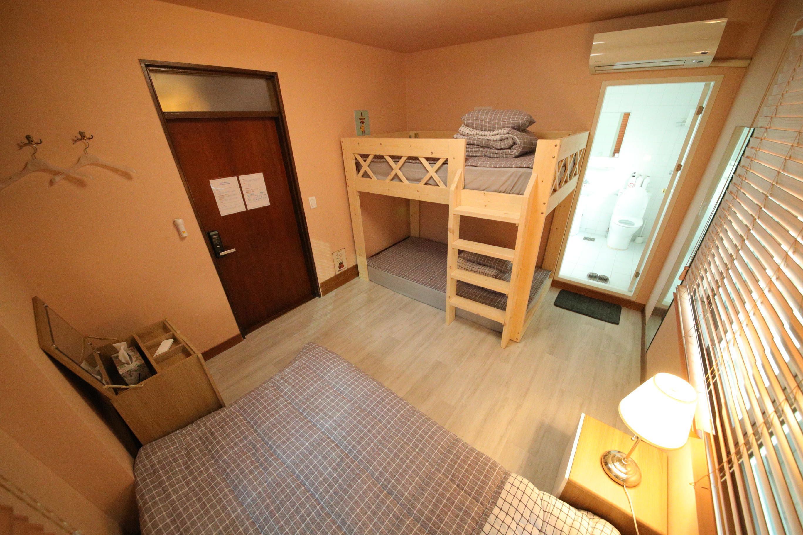 Una habitación con una cama individual superpuesta, un escritorio con lámpara, una puerta y una ventana con persianas.