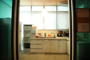 A compact kitchen with white cabinets, a microwave, a coffee maker, and a sink. - Stitches House - Hostel (Seoul)