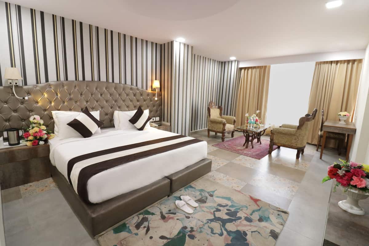A hotel room with a large bed, a sitting area with a chair and table, and a small desk with a lamp.