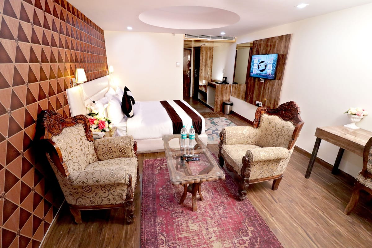 A hotel room with a sofa, two armchairs, a coffee table, a TV, and a mirror.