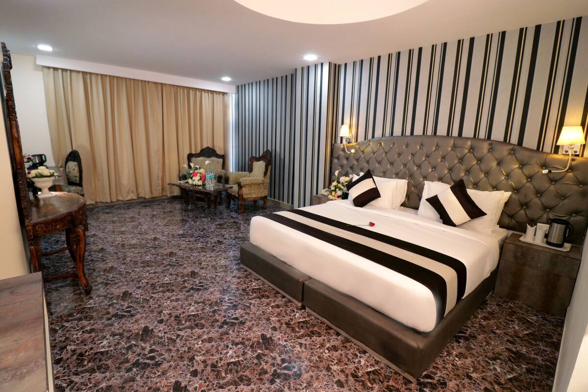 A hotel room with a large bed, a sitting area with a chair and table, and a decorative mirror.