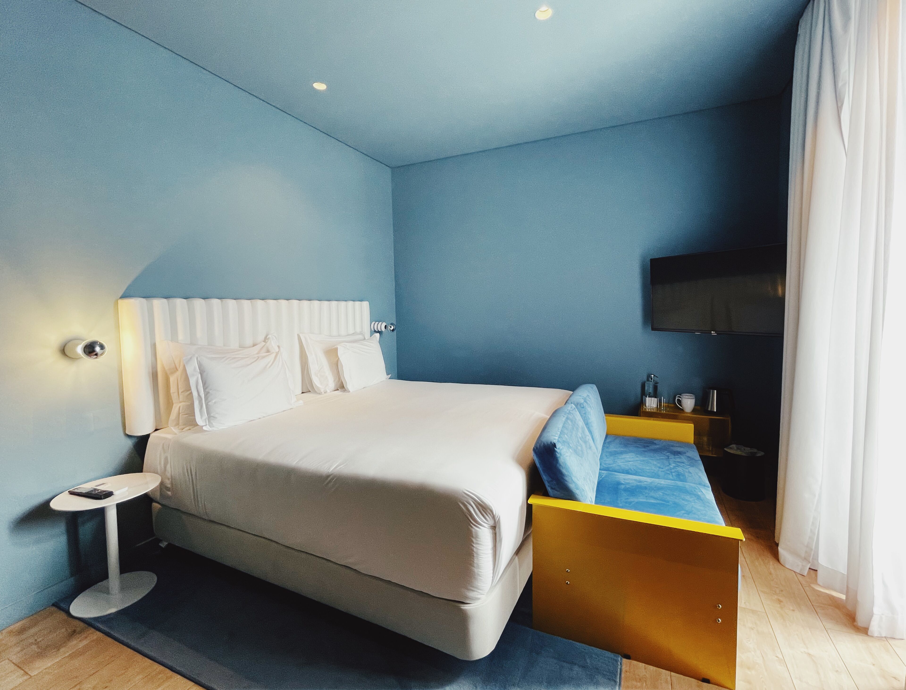 A modern bedroom with a large bed, bedside tables, a flat-screen TV, and a wooden floor.