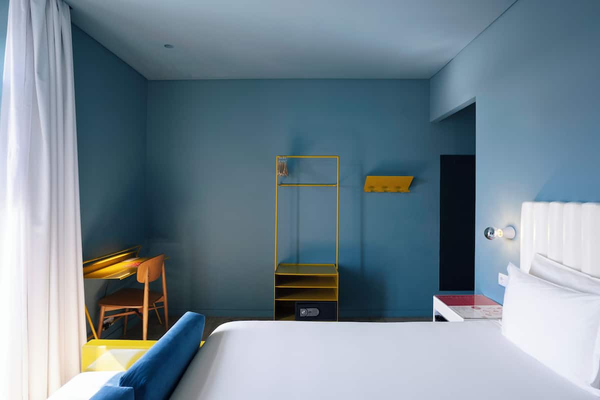 Een hotelkamer met een bed, een bureau, een stoel, een spiegel en een nachtkastje.
