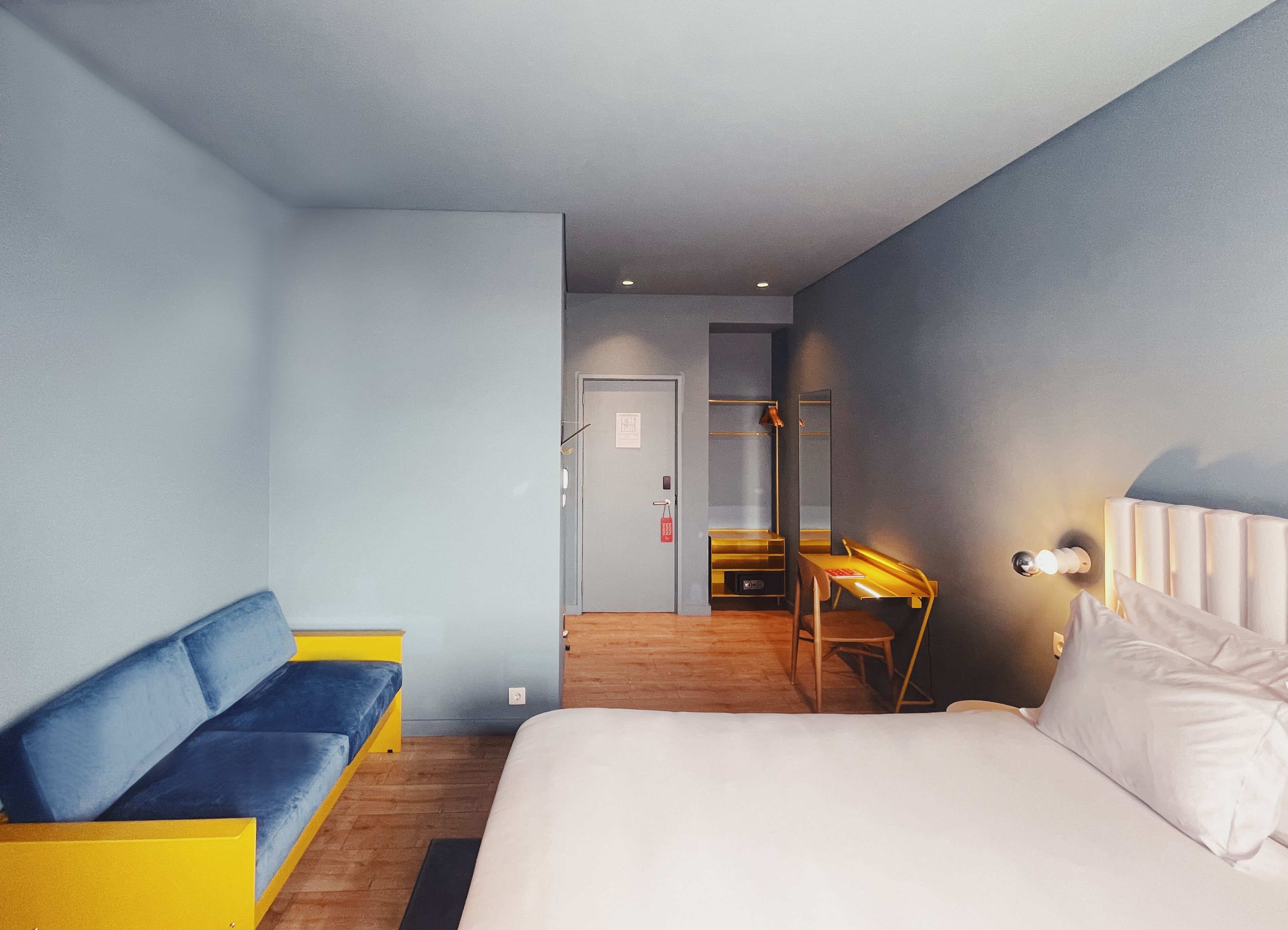 A modern hotel room with a large bed, a sofa, a desk, and a mirror.