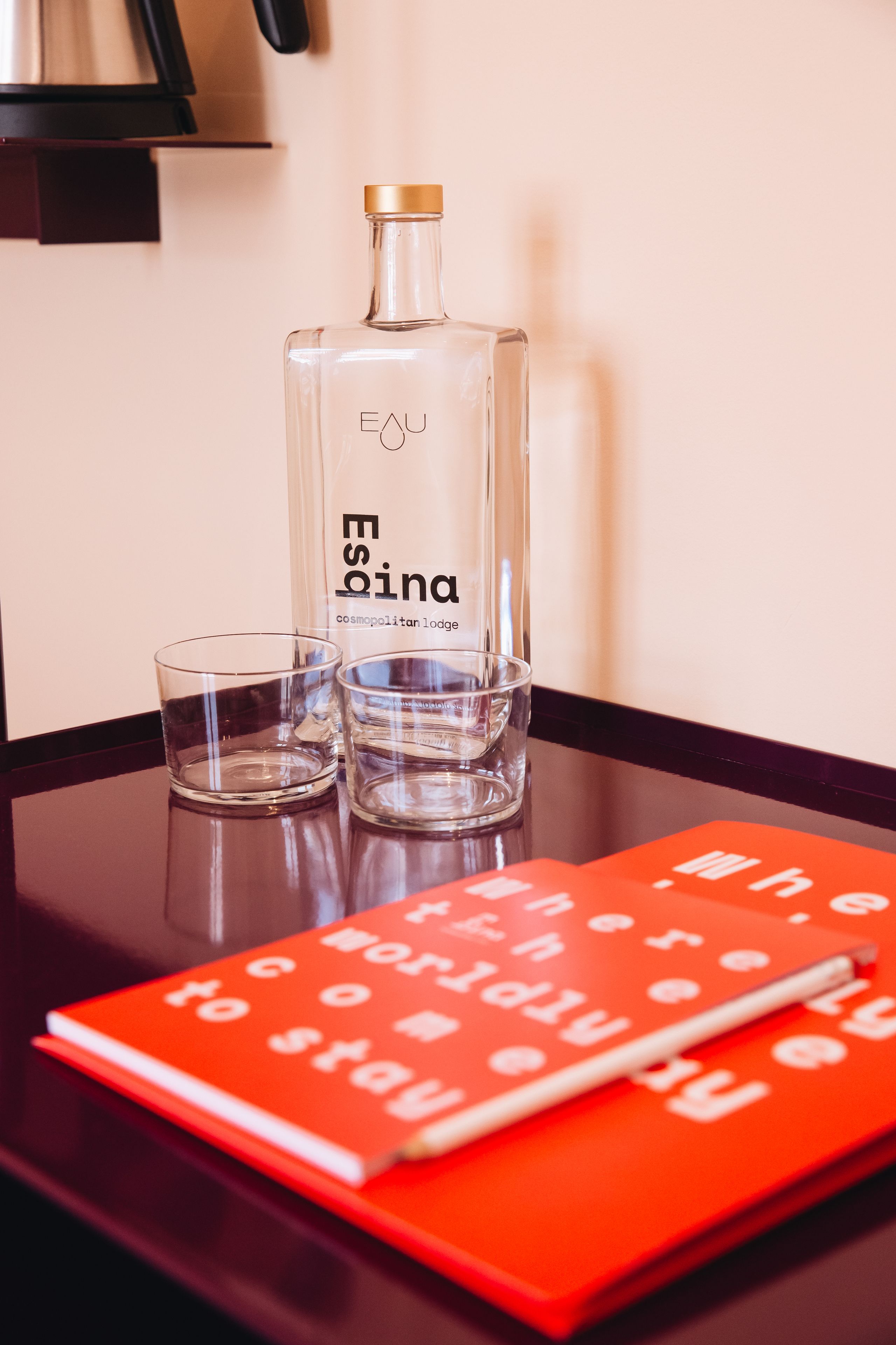 Eine Flasche des Eoina Cosmopolitan Lodge, zwei Gläser und ein rotes Notizbuch auf einem Tisch.