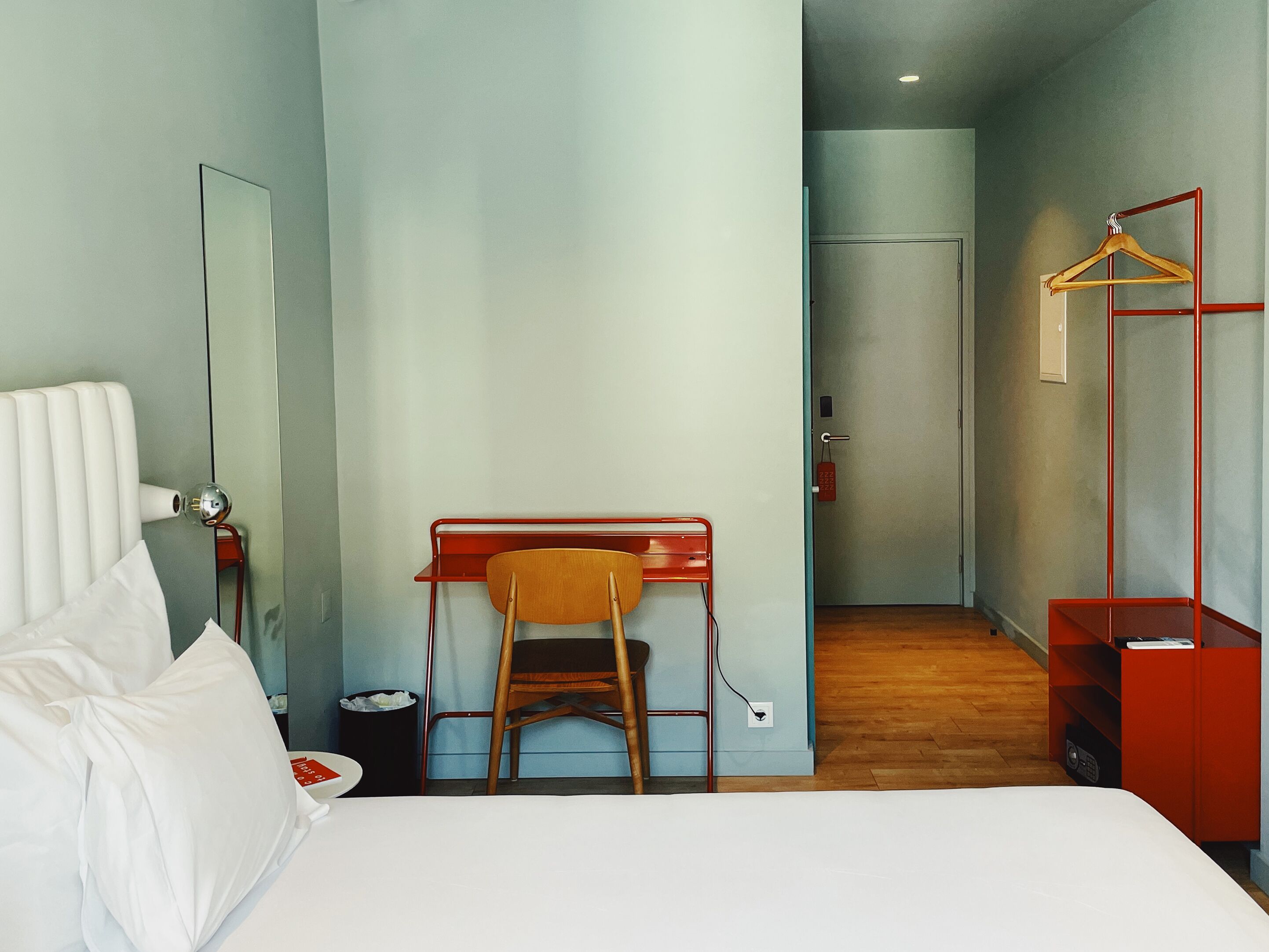 A hotel room with a bed, a desk, a chair, a wardrobe, and a mirror.