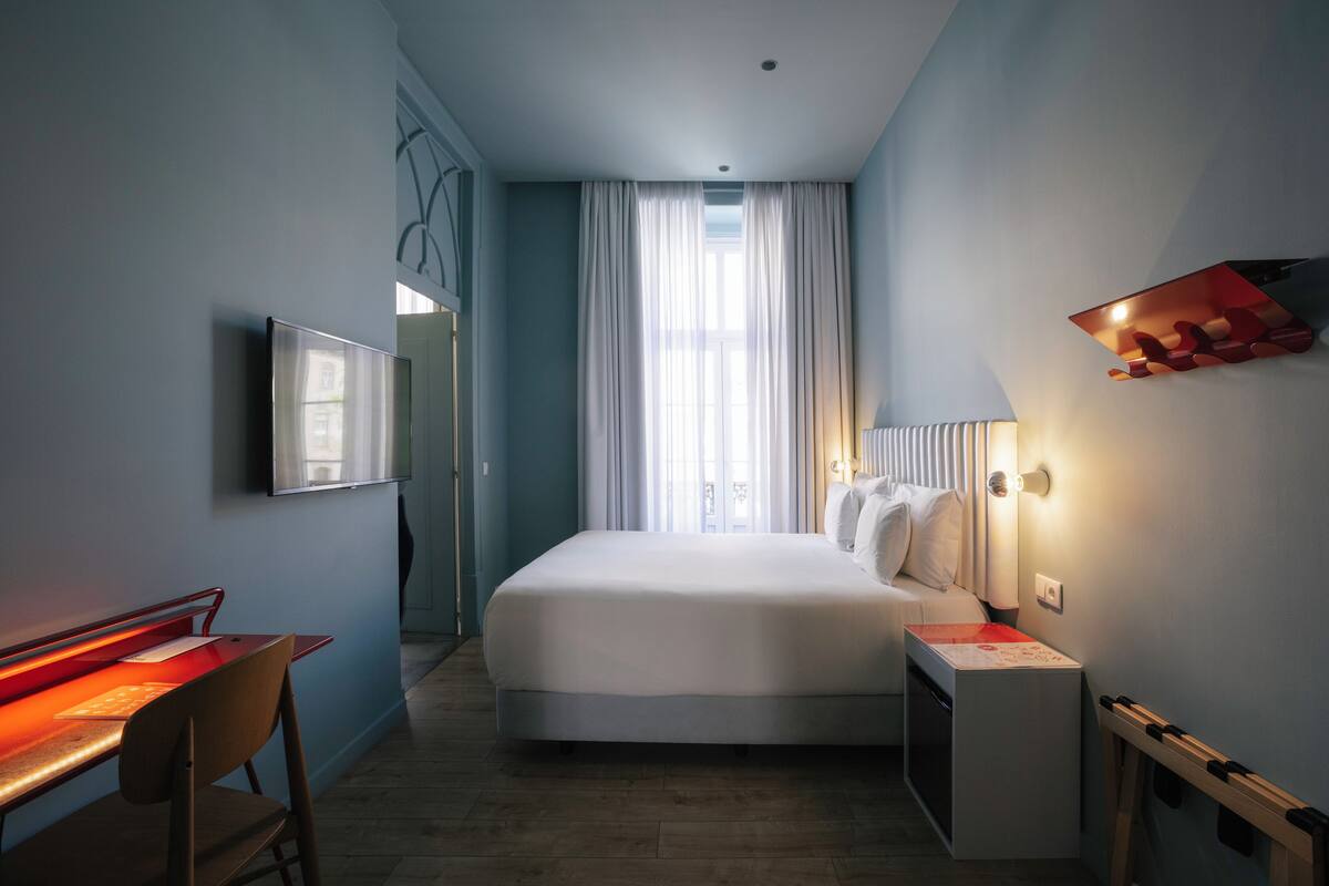Een moderne hotelkamer met een groot bed, een bureau met stoel, een aan de muur bevestigde televisie en een raam met gordijnen.