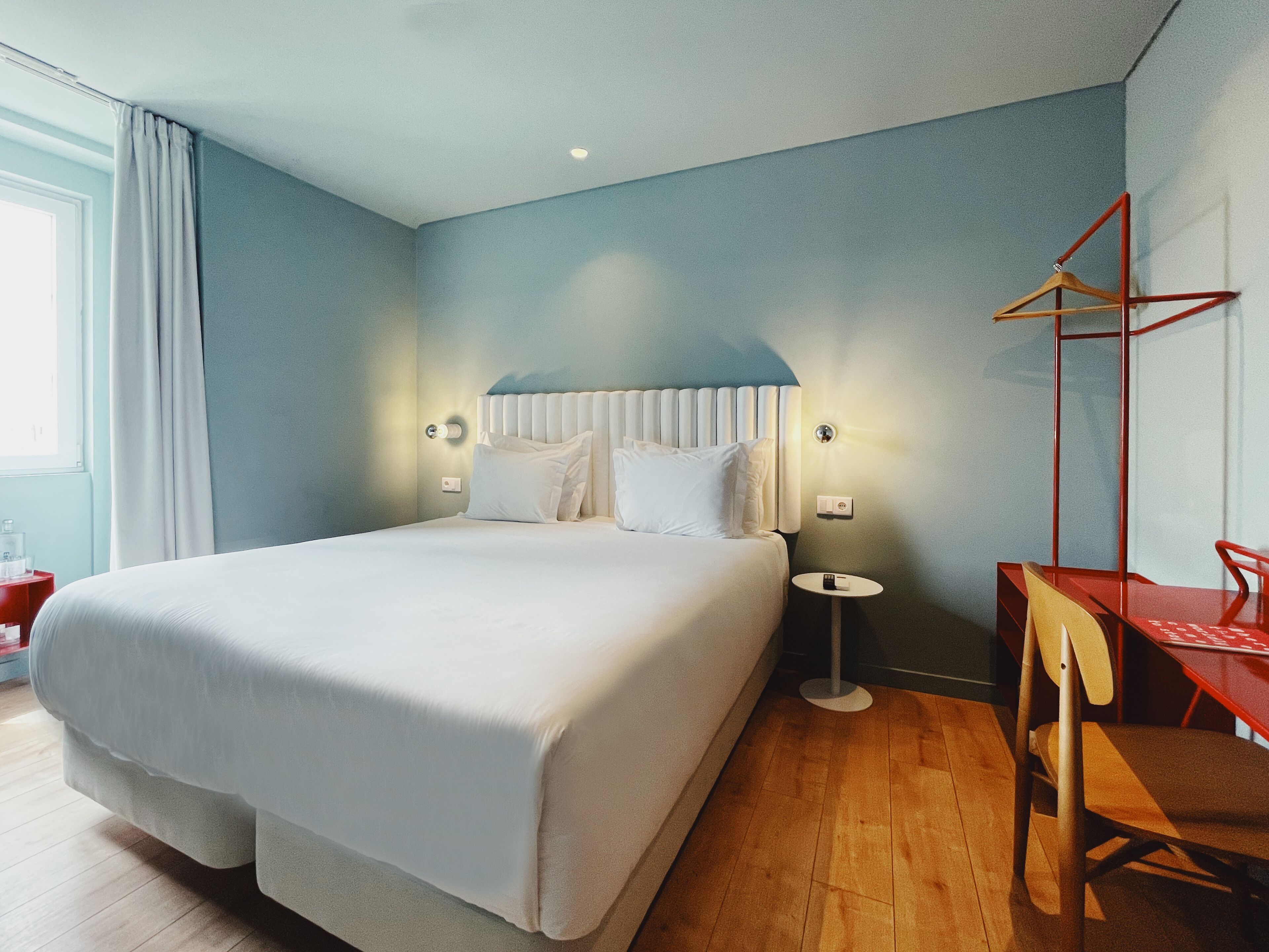 A modern hotel room with a large bed, bedside tables, a small desk, and a chair.