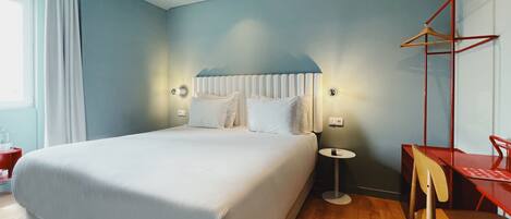 A modern hotel room with a large bed, bedside tables, a small desk, and a chair.