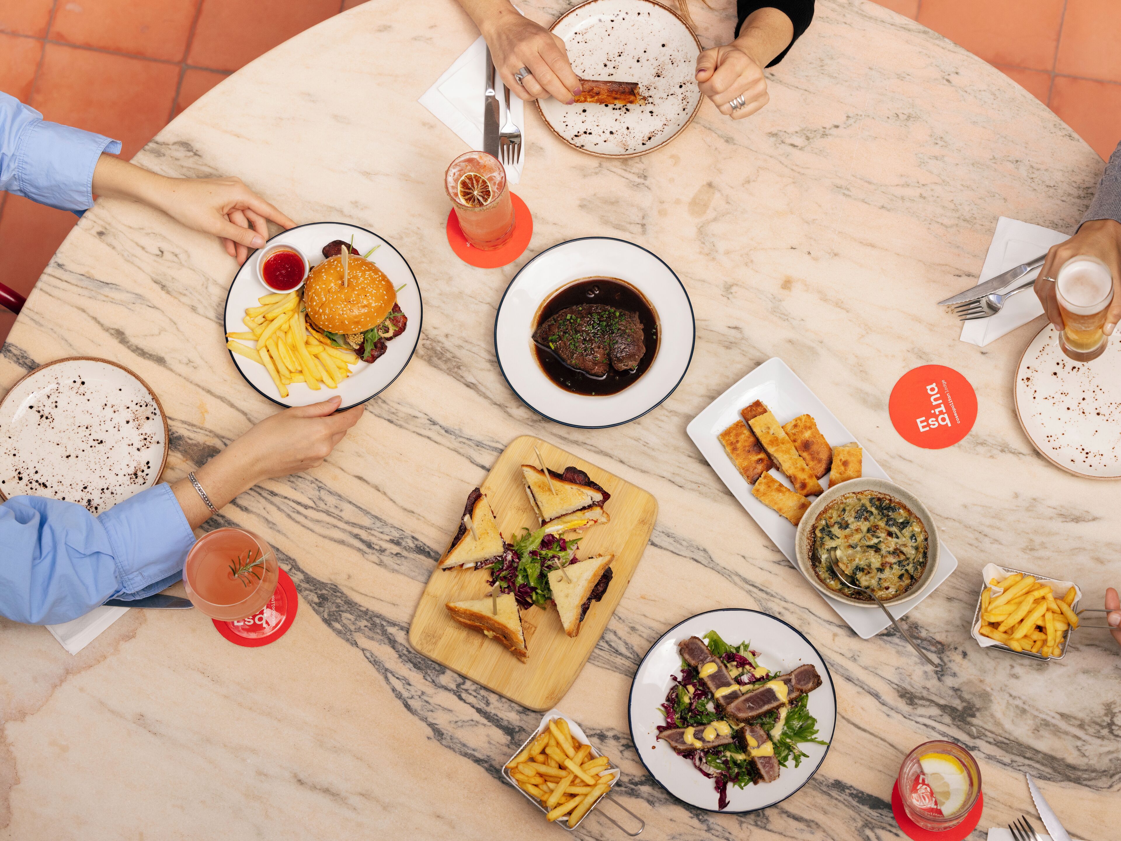 Une table ronde en marbre, sur laquelle on trouve différents plats, notamment un hamburger, des frites et une salade.