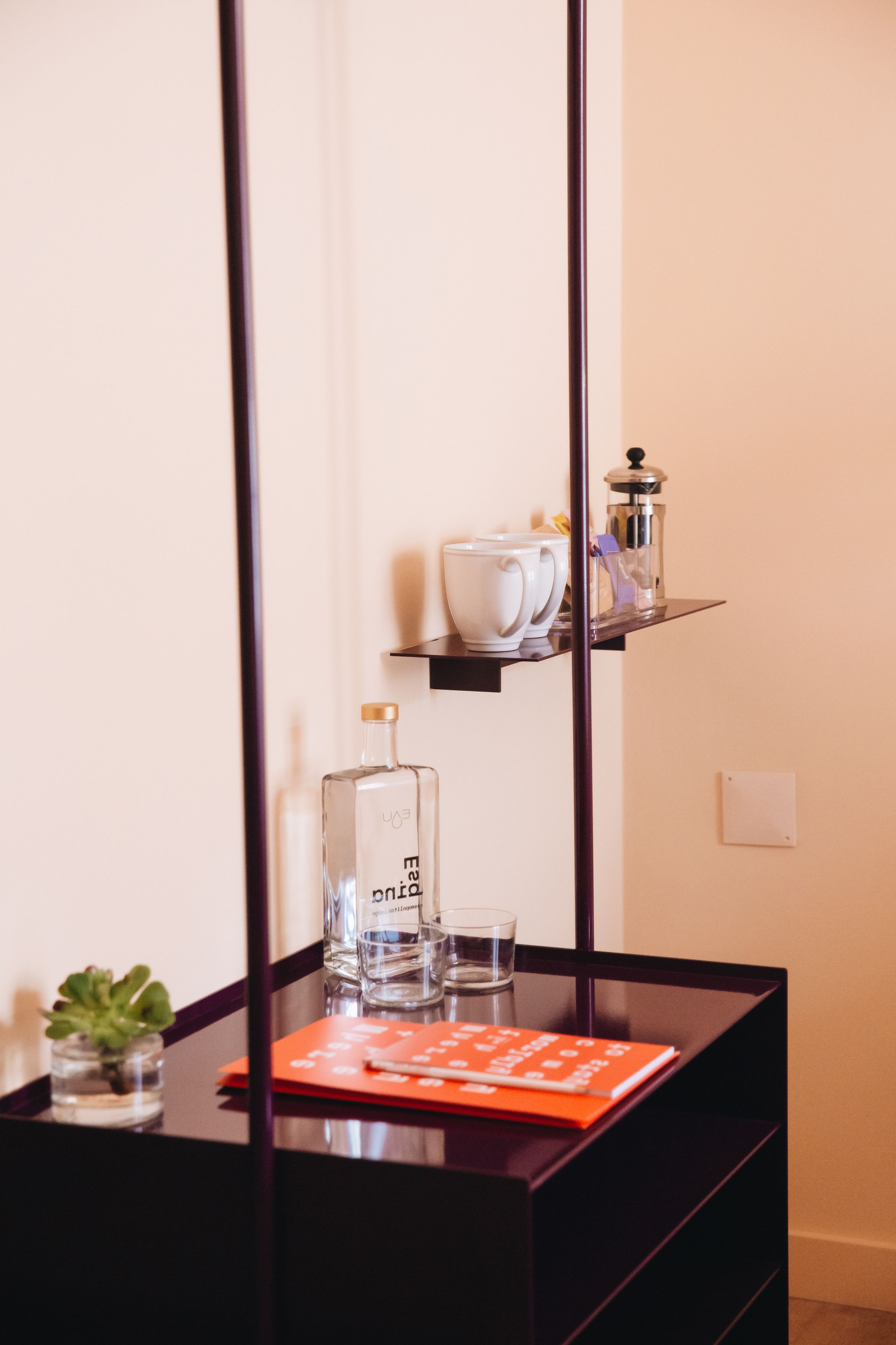 Una habitación moderna con un escritorio de madera oscura, una planta pequeña en maceta, una botella de vidrio y un cuaderno rojo.