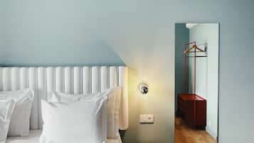 A hotel room with a bed, a bedside table, a mirror, and a wooden floor.