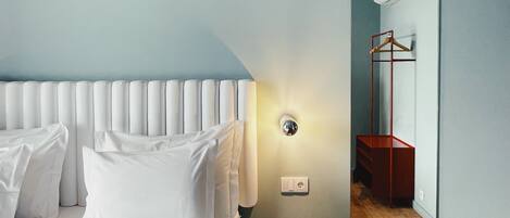 A hotel room with a bed, a bedside table, a mirror, and a wooden floor.