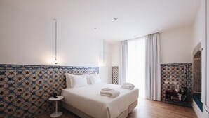 Una camera d'albergo con un letto grande, un tavolino piccolo, un comodino e vista all'esterno attraverso una finestra con tende.