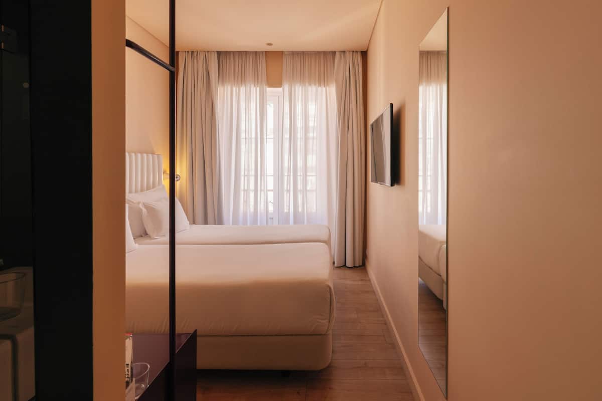Een hotelkamer met een groot bed, een flatscreen televisie en een raam met dunne gordijnen.